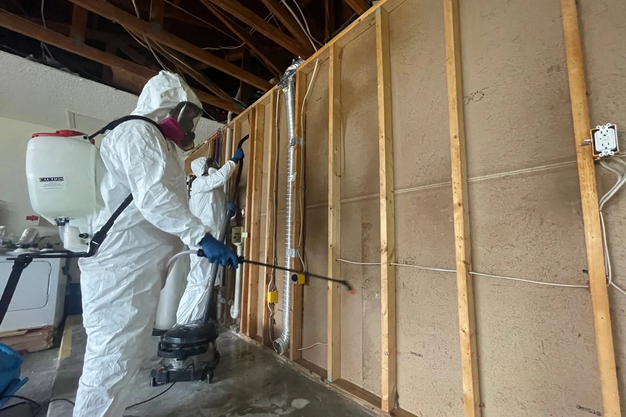 Two technicians in PPE treating exposed wall studs, American Quality Restoration